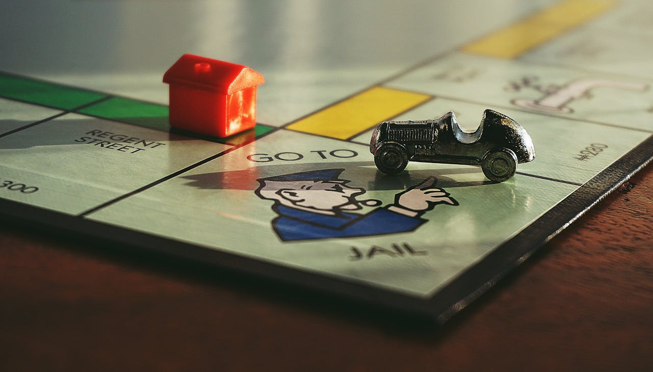 Close-up shot of a Monopoly board game featuring a toy car and a red house on Go to Jail.